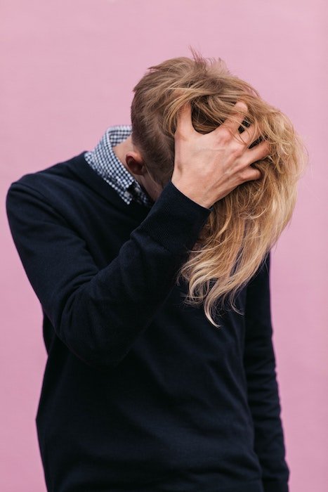 man posing while playing with hair against a pink background