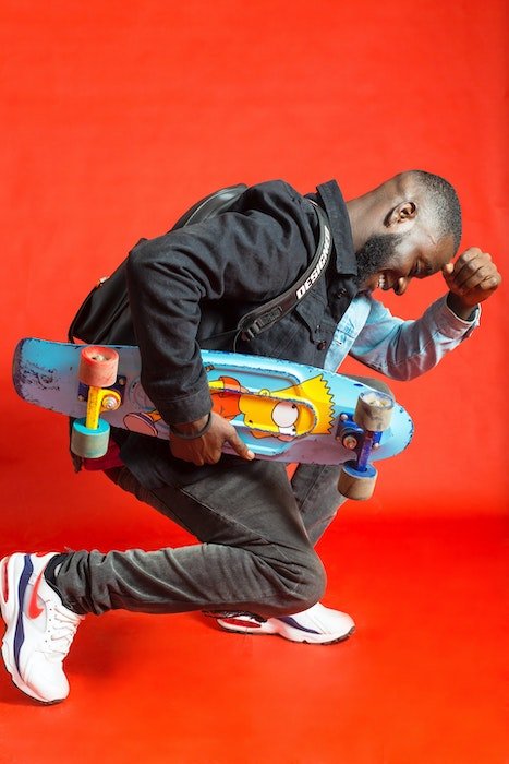Man posing agains a brighr red background with a skateboard