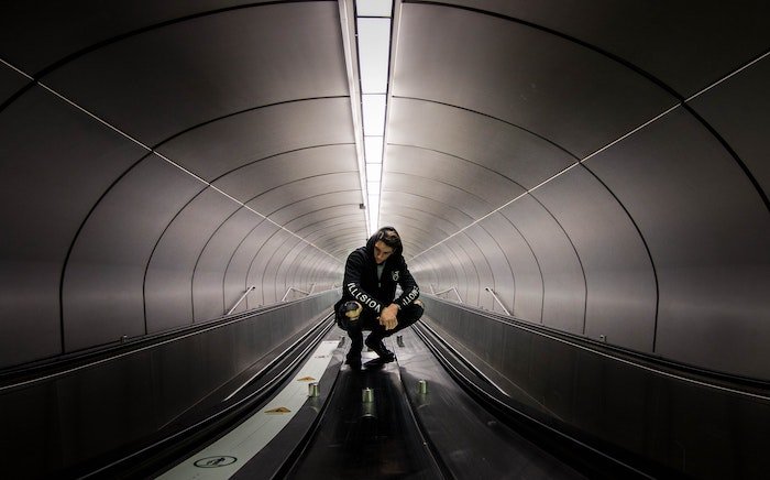 Man squats in underground tunnel with conveyor belts as an idea for male poses