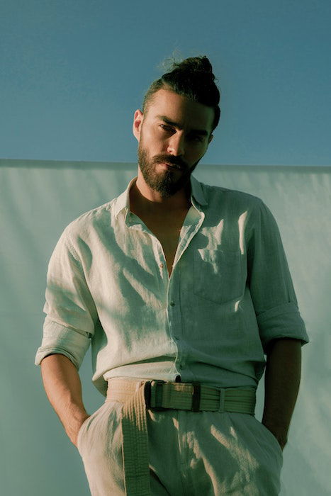 Man in light colored clothing posing with hands in his pockets 