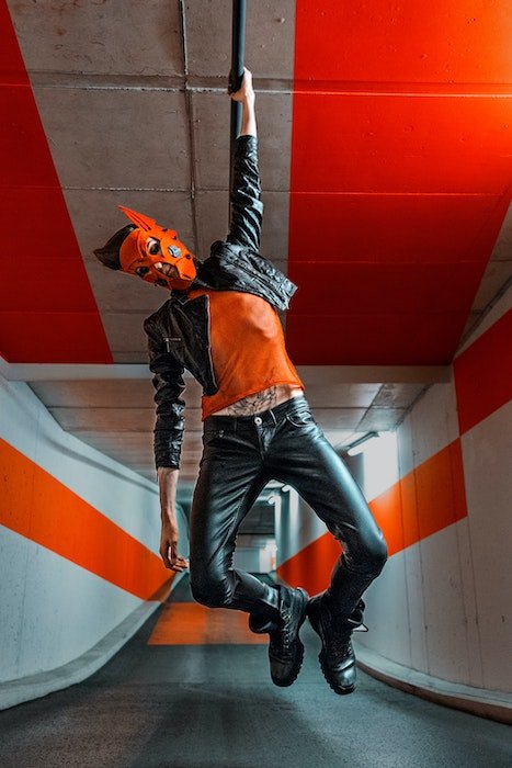 Full body shot of a man with a mask on hanging from a pipe in an underground tunnel