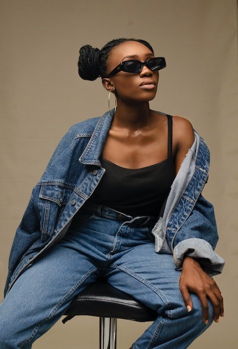 Model pose idea of a woman dressed in denim and sunglasses sitting in a studio chair