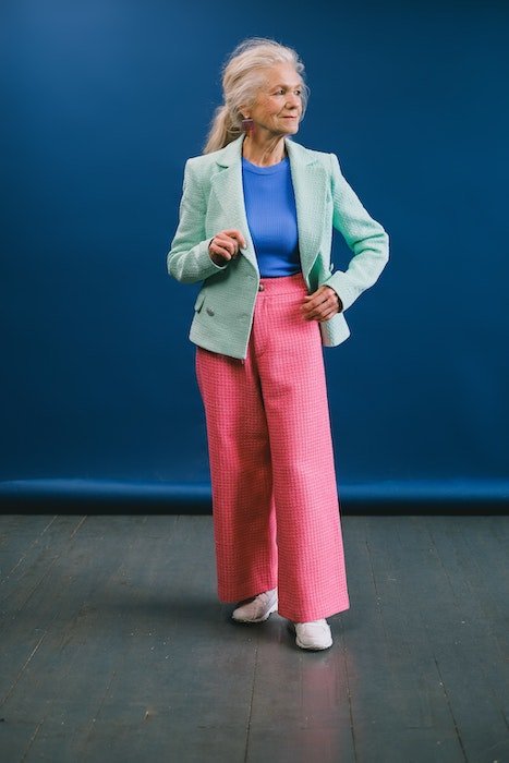 Full body shot of an older woman in a studio with bright clothes blue background and one foot forward as an example of model poses