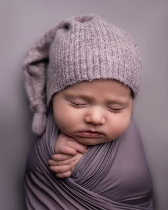 Baby wrapped in purple cloth with purple hat for a newborn photoshoot