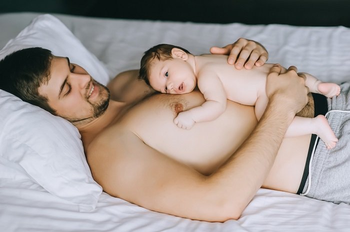 Baby lying on fathers chest on bed as a newborn photo example