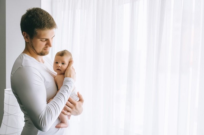 Father holding baby in a white room as newborn photo idea