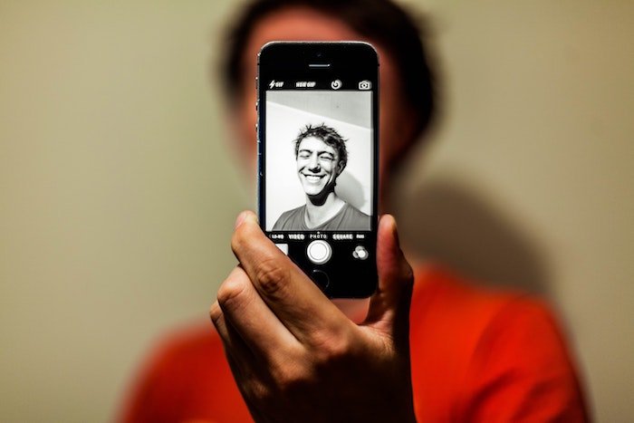 A phone shows a man making a selfie pose