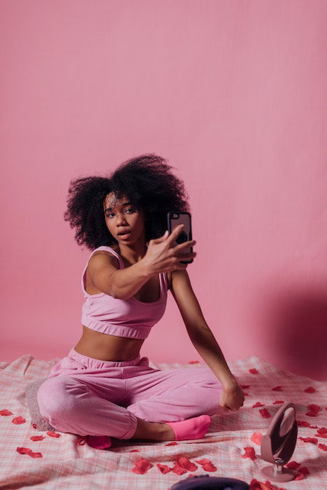 A woman sitting on a bed in a pink room taking a selfie