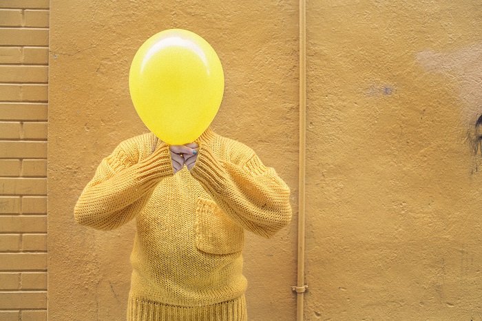 stock photo of a man in yellow jumper holding yellow balloon in front of his face
