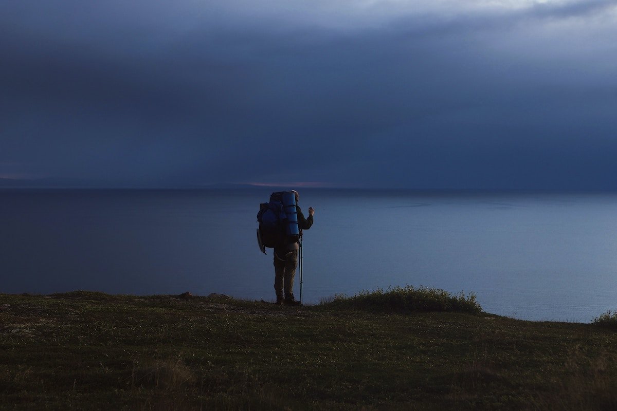 A hiker standing on a cliff above a large body of water on a dark cloudy day