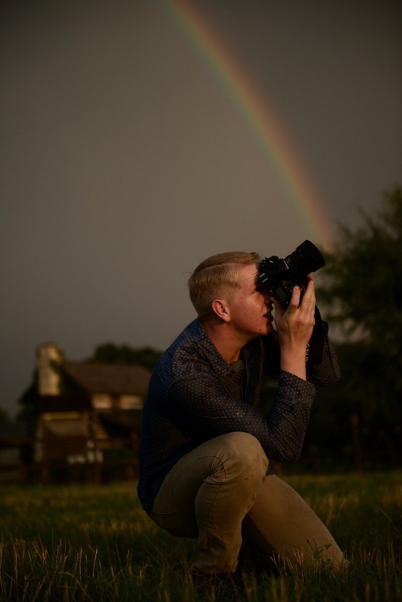 Photographer kneeling and taking a picture with a rainbow in the sky