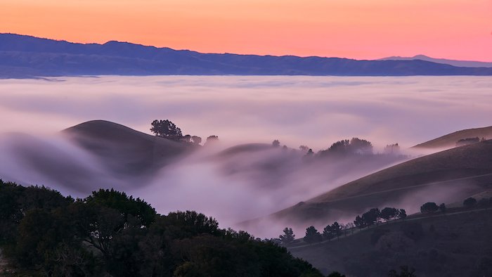 A long exposure shot of a foggy mountain at dawn