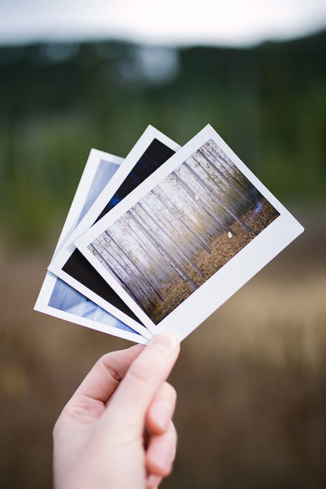 Uma mão segura três fotos brilhantes impressas