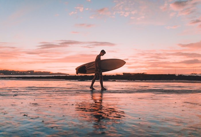surf photography example of a surfer walking on a beach at sunset