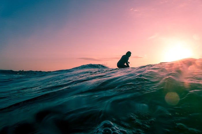 A surfer sits atop a surfboard at dusk
