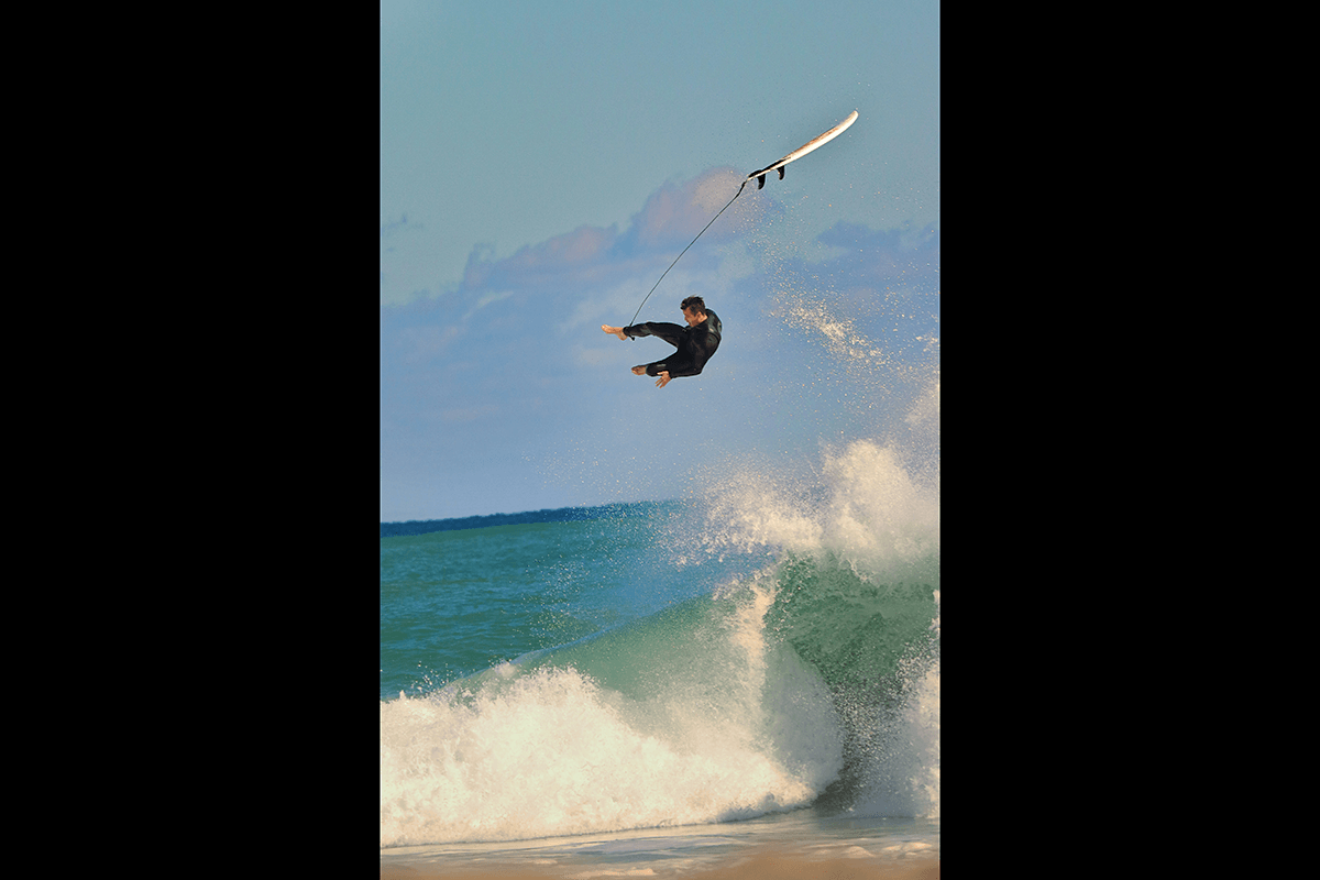 A surfer flying midair above a wave with a surfboard attached as an example of surf photography