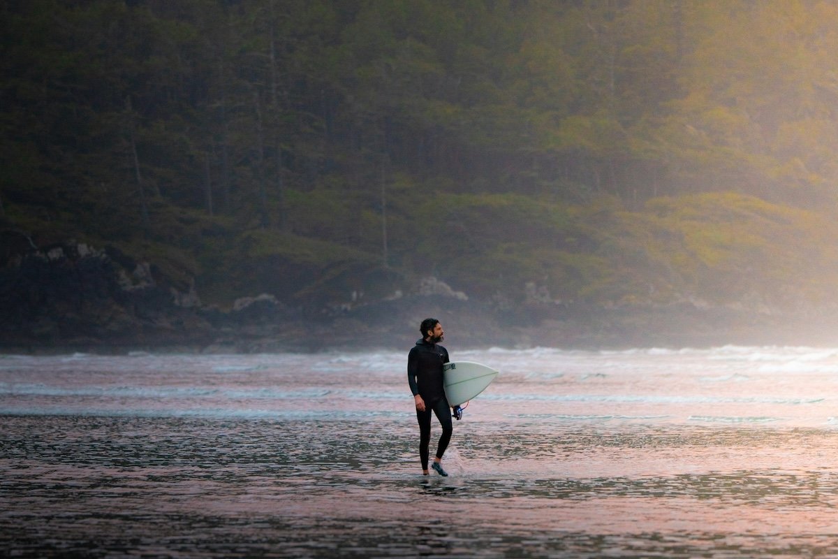 A surfer walking with his surfboard in a wetsuit on the shore as an example of surf photography
