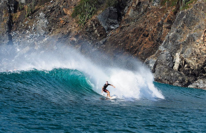 surf photography example of a surfer riding a crashing wave with a sea cliff in the background