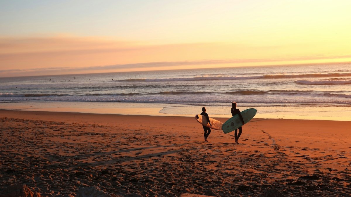 Two surfers with surfboards walking towards the ocean at sunset as an example of surf photography