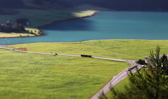 A miniature shot of a lake and field, with tiny cars driving on a road