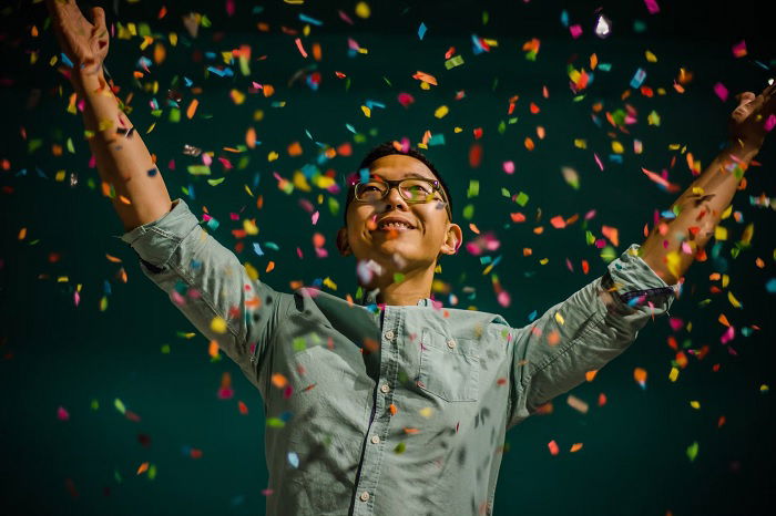 Young man with glasses with arms raised under a shower of confetti