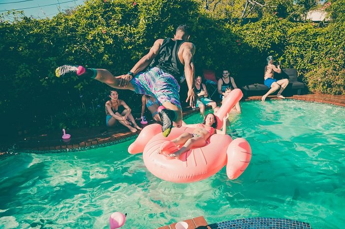 Man jumping into a pool where a woman on an inflatable is floating