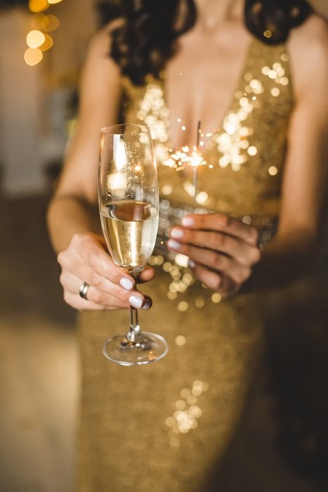Woman in a gold dress holding a champagne glass and sparkler 