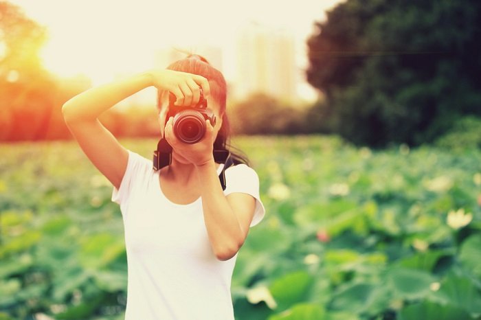 A photo of a woman taking a photo in a field as the sun sets