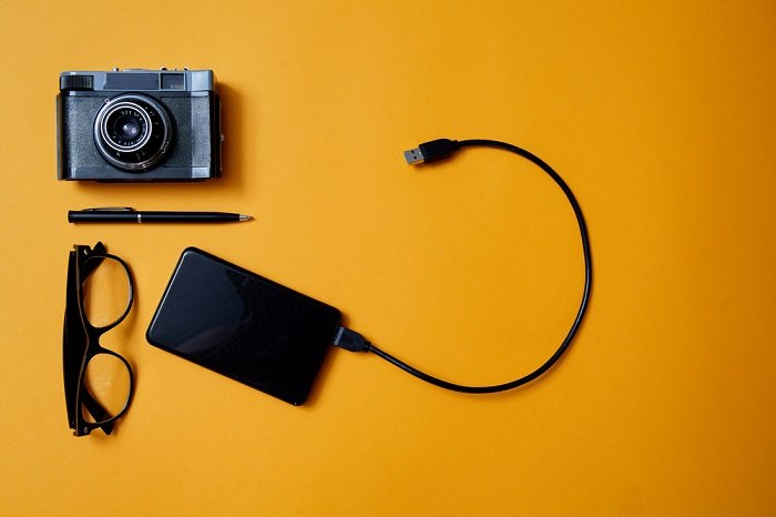 Camera, hard drive, and glasses on an orange backdrop