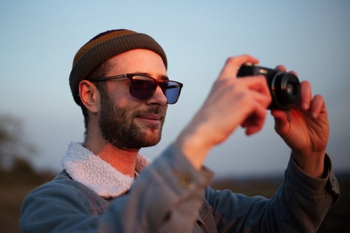 Man in a wool hat taking a picture with a compact camera