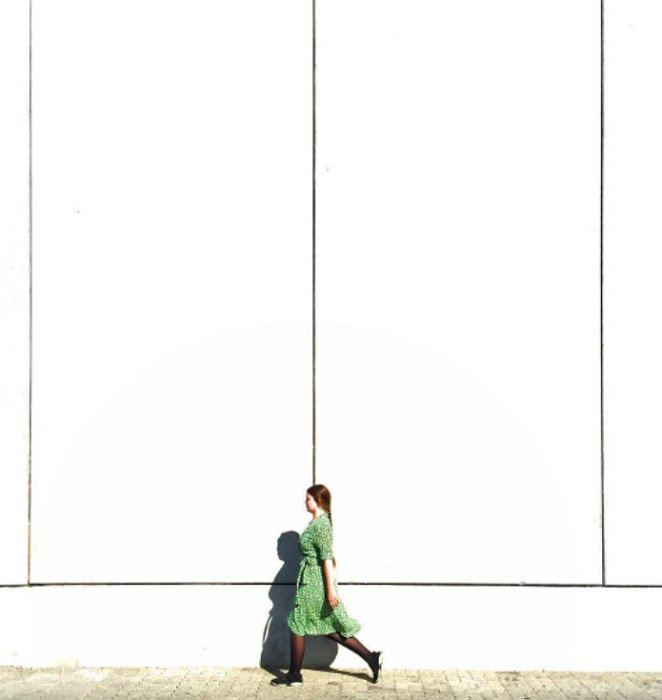 Mulher de vestido verde andando em frente a uma parede branca, criando uma forte ênfase na foto
