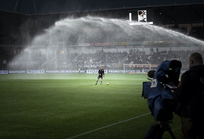 Footballer on the pitch while sprinkler is sprinkling