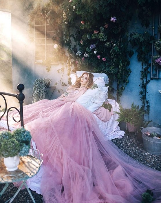 一个穿着粉红色大裙子的女人躺在床上，作为幻想摄影的一个例子