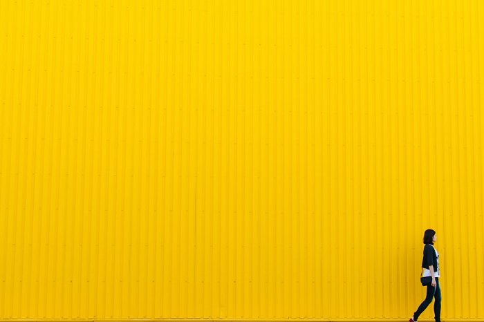 Woman walking in front of a yellow wall, as an example of minimalist photography