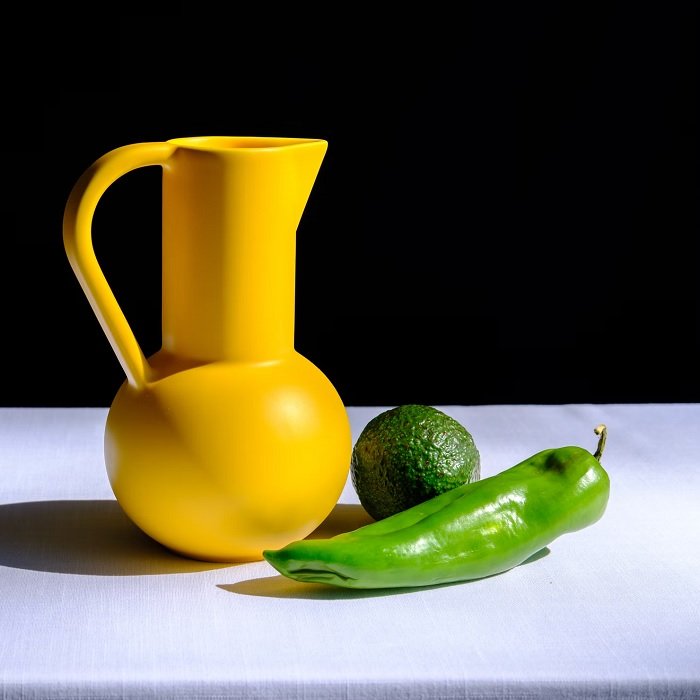 Still life photo of a yellow jug, a lime, and a chili pepper