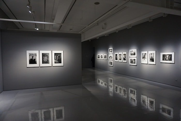 A photograph of a photography exhibition. Soft light illuminates black and white photos displayed on the wall.