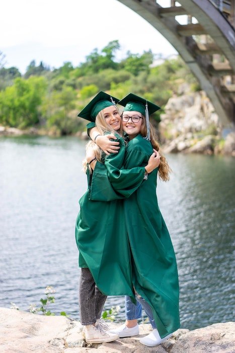 Two senior high-school graduates in caps and gowns hugging for a senior picture