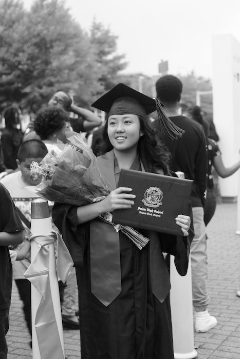 Black and white photo of a senior high-school graduate holding flowers and her diploma
