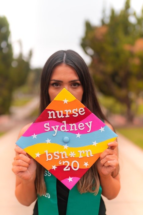 A girl holding up a colorfully decorated grad cap with words and numbers on it