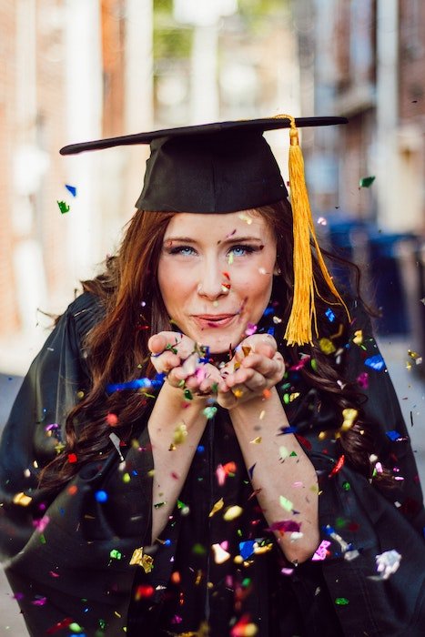 A high school graduate blowing confetti out of her hands as an example of a unique senior picture idea
