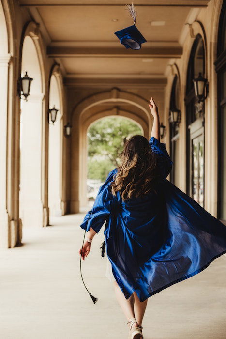 Back of a graduate walking down an outdoor passageway and throwing their cap in the air