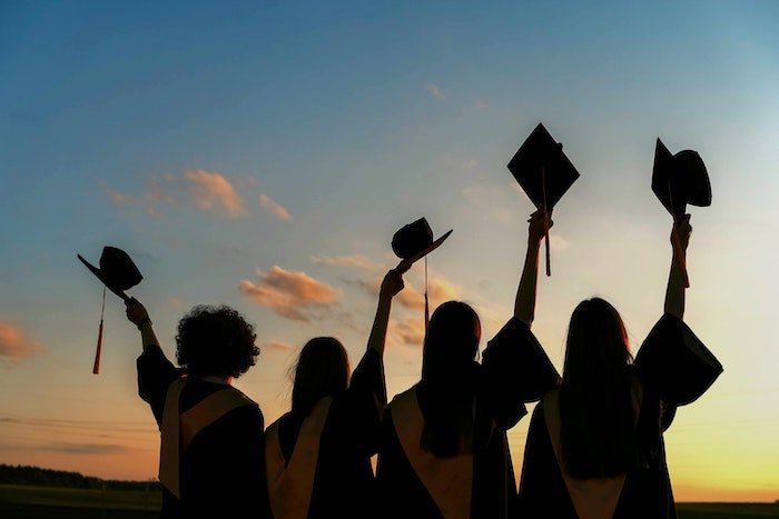A senior picture idea with a silhouette of four senior high-school graduates raising their cap in the air