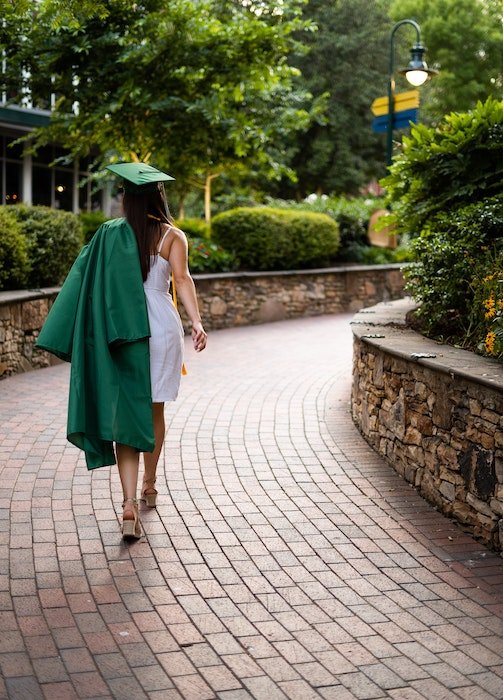 Back of a senior high-school graduate with a cap and gown walking down a brick walkway as an example of senior picture ideas