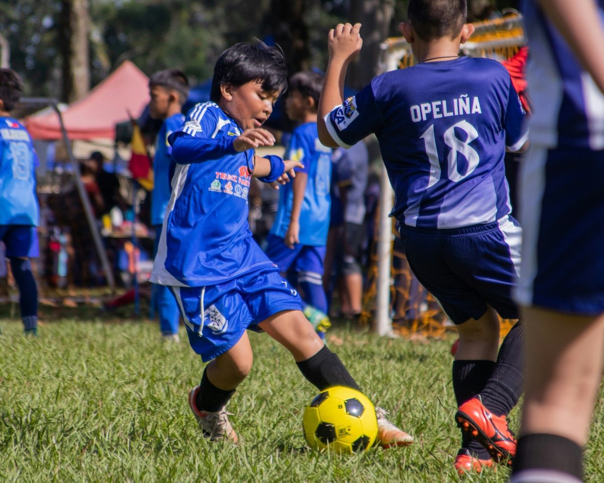 A kid dribbling a soccer ball in a football match to show photography settings