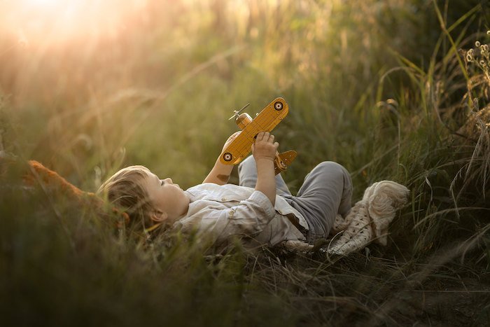A child lying down in grass playing with a toy plane