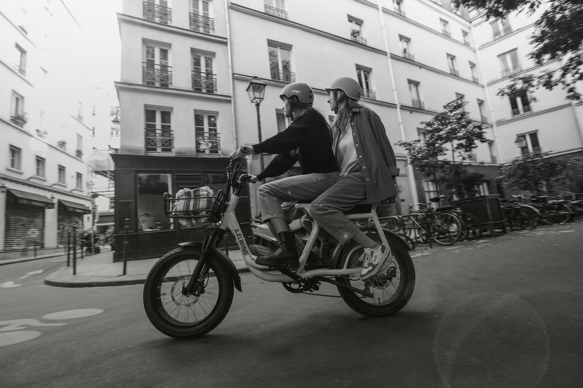 A black-and-white photo of two women riding on a moped shot with an f/6.3 aperture