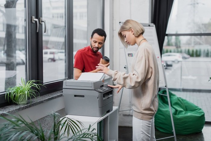 Woman using a printer in a modern office space near a man having a coffee