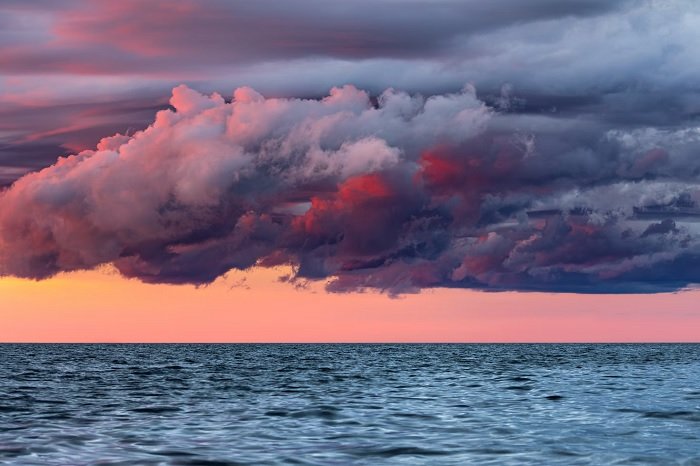 Dark clouds in front of an orange sky over a clam sea