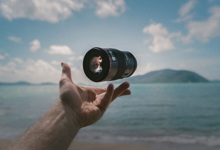 Camera lens being thrown in the air by a hand in front of a coastal scene