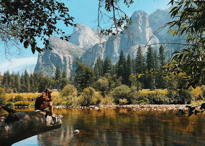 Girl sitting on log over a river with mountains beyond